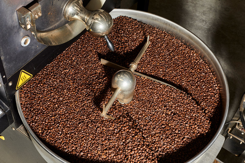Roasted coffee beans being stirred by the arms of the roaster