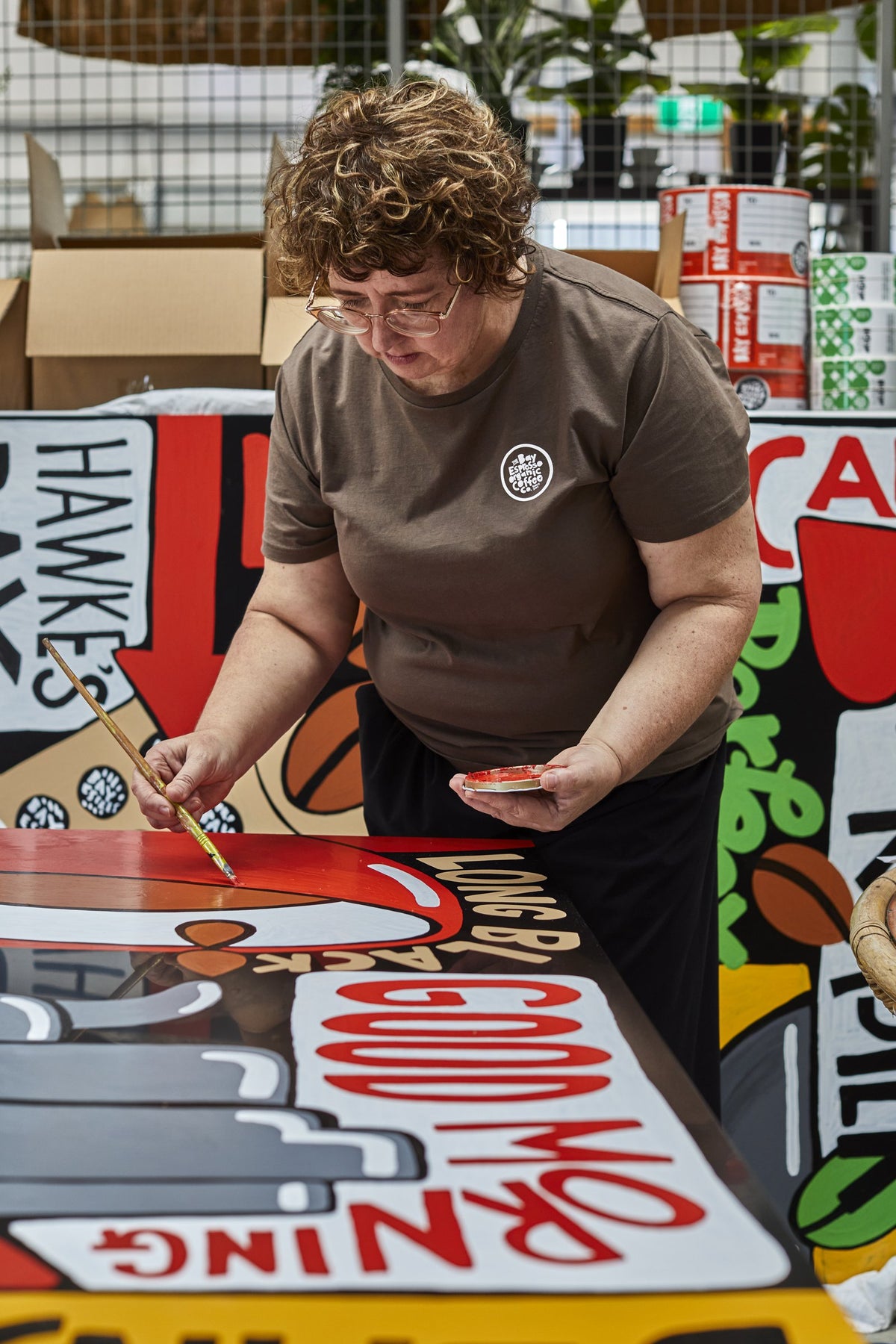 Jonelle painting a red detail on one of the Bay Espresso mural panels